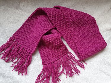 Gestrickter fuchsiafarbener Kinderschal mit Fransen auf hellem Untergrund