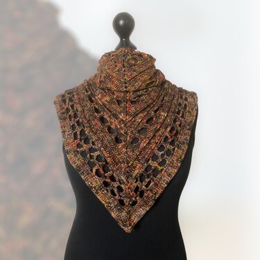 Crocheted triangle shawl with openwork lace in variegated rust, brown, and olive yarn on a black dress form.