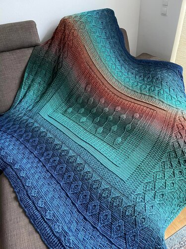Ombre crochet throw in shades of blue and coral with leaf motifs, cables and diamond borders