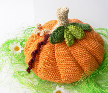 orange crocheted pumpkin plush with beige stem and green leaves on green raffia