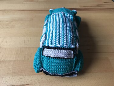 Handgehäkeltes Amigurumi-Auto in türkis, weiß und hellgrau, Draufsicht auf Holzoberfläche.