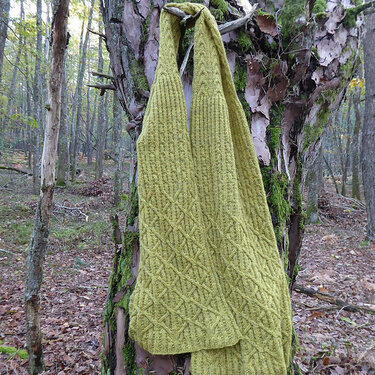 Olivgrüner Loop-Schal mit Zopf- und Rautenmuster an einem Baumstamm