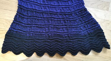 Handgehäkelter Poncho in Blau bis Dunkelblau mit Wellenkante, flach auf hellem Holzboden gelegt