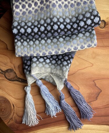 Loop-Schal mit kleinen mehrfarbigen Motiven und vier Quasten auf Holzuntergrund