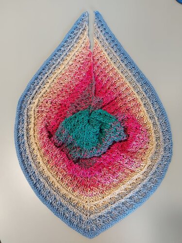 Gehäkeltes Dreieckstuch in Verlaufsgarn mit grüner Mitte, rosa und beigen Zwischenringen und blauem Rand, flach auf Tisch gelegt