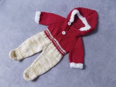 Gestrickter Baby-Strampler in Rot und Beige mit Kapuze, weißen Knöpfen und flauschigem Besatz auf neutralem Untergrund.