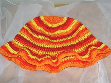 Nahaufnahme einer gestreiften, gehäkelten Kindermütze mit welligem Saum in Gelb, Orange und Rot