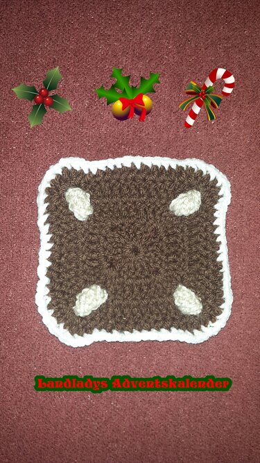 Braunes gehäkeltes Quadrat mit weißem Zierrand und vier hellen Eckapplikationen, auf einem rötlich-texturierten Hintergrund, dekoriert mit weihnachtlichen Stickern oben.