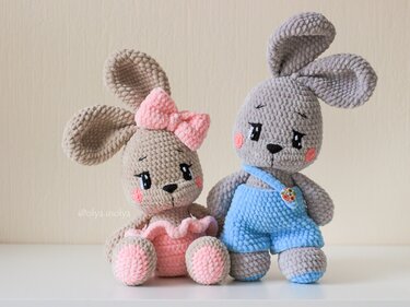 Two amigurumi crochet bunnies: left beige with pink bow and ruffled skirt; right gray in blue overalls with a button.