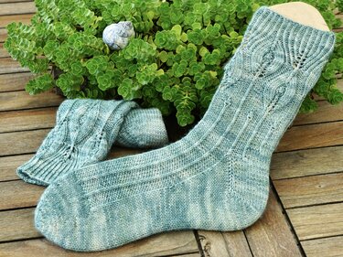 Seafoam-green knitted socks with lace leaf cable pattern beside a succulent on wooden planks