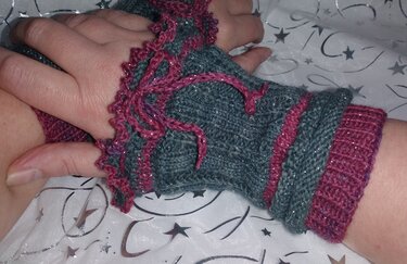 Nahaufnahme von Händen mit dunkelgrauen, fingerlosen Armstulpen mit magentafarbenen Rüschen und Glitzerfaden.