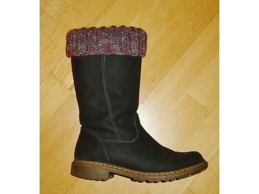 Schwarzer Stiefel mit umgeschlagener mehrfarbiger Strickstulpe auf hellem Holzboden