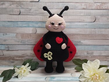 Gehäkeltes Marienkäfer-Amigurumi mit roten Flügeln, Herz und kleinem Kleeblatt