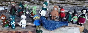 Mehrere bunte, handgehäkelte Amigurumi-Figuren (Wichtel, Elfen) und ein großer blauer Vogel auf Holzstämmen.