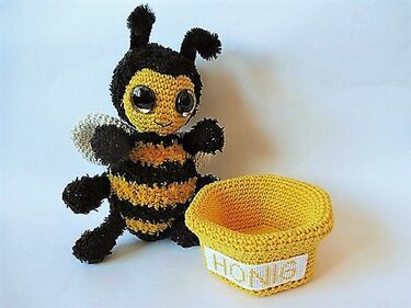 Gehäkelte gelb-schwarze Amigurumi-Biene neben kleinem Honigtopf