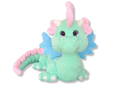 Mint-green crocheted amigurumi dragon with pink horn and blue wings