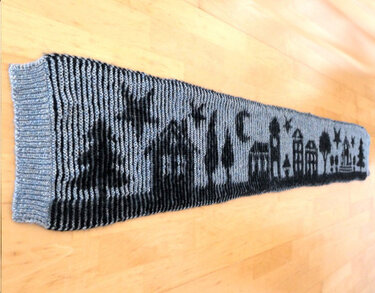 Langer gestrickter Schal mit schwarz-grauem Stadtsilhouettenmuster auf Holzboden