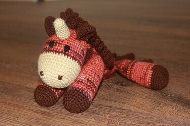 Gehäkeltes Amigurumi-Einhorn liegend, rot-braun gestreift mit cremefarbener Schnauze und brauner Mähne