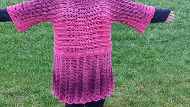 Rückenansicht eines gehäkelten Damenkleids in Pink bis Purpur mit ausgestelltem Rock und weiten Ärmeln