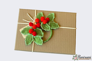 Textured brown gift box with crocheted green holly leaves and red berries tied with white string