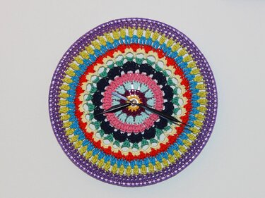 Runde Wanduhr mit buntem gehäkeltem Mandala und schwarzen Uhrzeigern