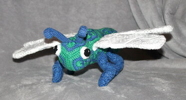 Gehäkeltes Amigurumi-Insekt blau-grün mit weißen Flügeln und auffälligen Augen