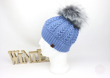 Light blue crocheted beanie with cable-style stitch, ribbed brim, and gray faux fur pom-pom on a white mannequin head.