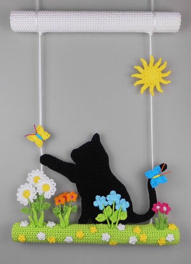Crocheted wall hanging: black cat silhouette, green floral base, colorful flowers, butterflies, and sun