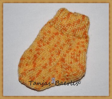 Handgestrickte Babysocke in gelb-orange Melange mit Rippenbündchen auf hellem Hintergrund.