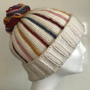 Weiße gestrickte Damenmütze mit Umschlagbündchen, bunten Längsstreifen und mehrfarbigem Bommel