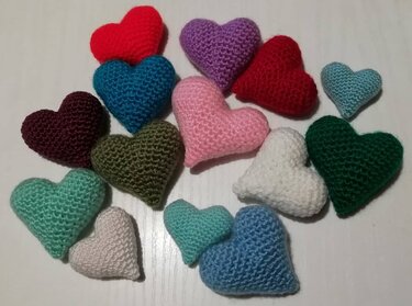 Mehrere gehäkelte, gefüllte Herzen in unterschiedlichen Farben auf hellem Untergrund