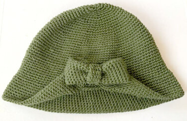 Eleganter gehäkelter Cloche-Hut in gedecktem Grün mit Schleife, auf hellem Hintergrund präsentiert.