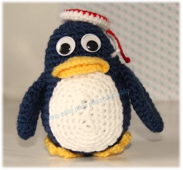 Gehäkelter Pinguin-Amigurumi in Dunkelblau mit weißem Bauch, gelbem Schnabel und rot-weiß gestreifter Matrosenmütze