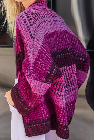Seitenansicht einer Oversize-Strickjacke mit offenem Maschenbild und horizontalen Farbblöcken in Pink- und Beeretönen