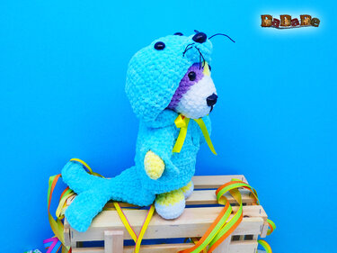 Gehäkelter Amigurumi-Hund im hellblauen Robbenkostüm auf Holzkiste vor blauem Hintergrund
