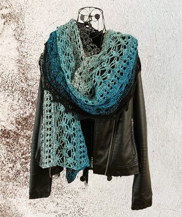 Teal-to-black gradient crochet lace scarf draped over a black leather jacket on a wire mannequin