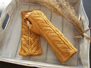 Senfgelbe gestrickte fingerlose Armstulpen mit Ajour-Blattmuster auf Holztablett
