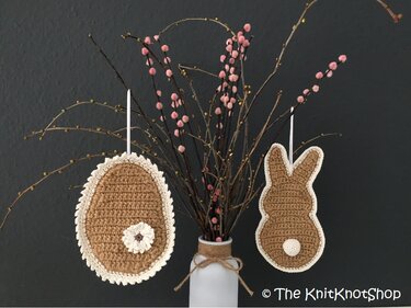 Gehäkeltes Osterei und Hase zum Aufhängen, braun mit cremefarbener Umrandung, an Zweigen in Vase