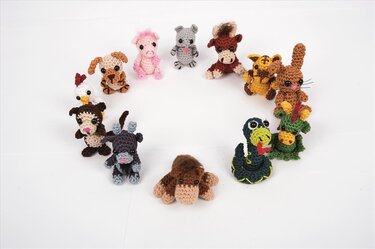 Zwölf gehäkelte Amigurumi-Tiere — darunter Schwein, Maus, Ochse, Tiger, Hase, Drache, Schlange, Pferd, Ziege, Affe, Hahn und Hund — angeordnet in einem Kreis auf weißem Grund.