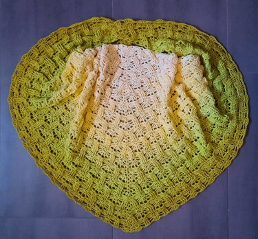 Gehäkeltes Dreieckstuch mit Farbverlauf von Creme über Gelb zu Grün, flach auf dunklem Untergrund.