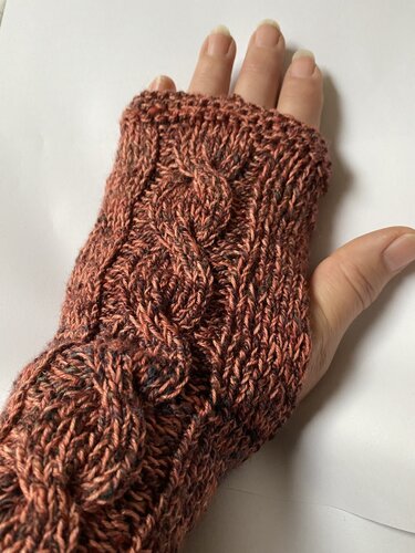 Gestrickte rostrote, fingerlose Armstulpe mit Zopfmuster an einer Hand