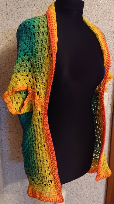 Gehäkelte Damenweste in Grün, Gelb und Orange mit Ajourmuster und kurzen Ärmeln auf einer schwarzen Schneiderbüste.