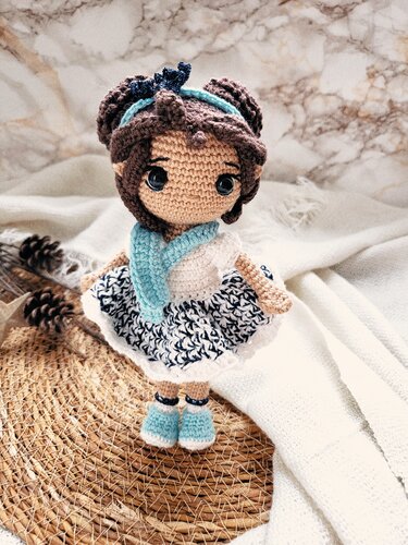 Gehäkelte Amigurumi-Puppe mit braunem Haar, hellblauem Schal und blau-weißem Kleid.