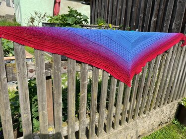 Gehäkeltes Dreieckstuch mit Rot‑Blau‑Farbverlauf über einem Holzzaun
