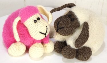 Zwei gehäkelte Amigurumi-Schafe, eines rosa, eines creme mit braunen Details