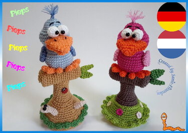 Zwei gehäkelte Amigurumi-Vögel (hellblau und rosa) auf gehäkelten Baumstümpfen mit grüner Basis.