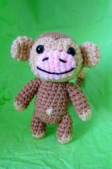 Gehäkelter Amigurumi-Affe, braun mit rosa Schnauze vor grünem Hintergrund