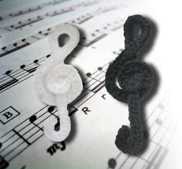 Zwei gehäkelte Violinschlüssel (weiß und dunkelgrau) auf einem Notenblatt.