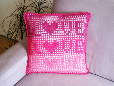 Rosa gehäkeltes Kissen mit LOVE‑Schriftzug und Herzmotiven auf einem Sofa