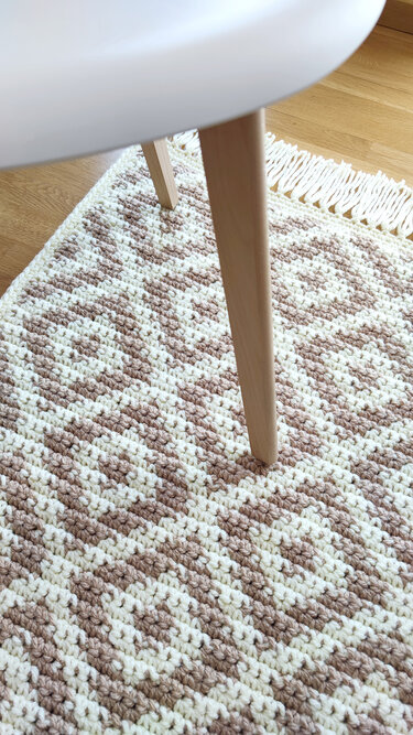 Gehäkelter Teppich in Creme und Taupe mit Rautenmuster und Fransen, Teilansicht unter Stuhlbein
